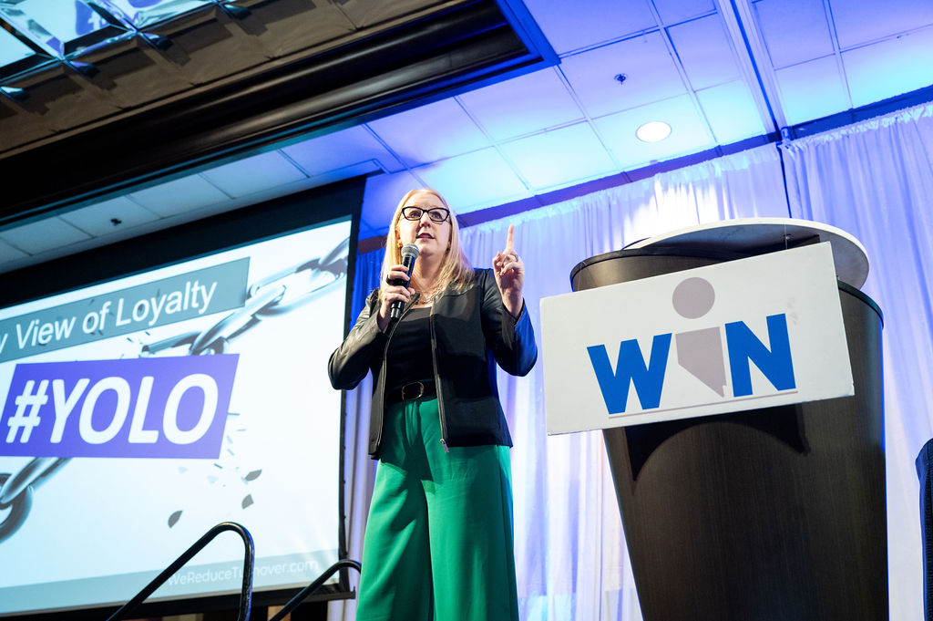 blonde woman on stage speaking on microphone
